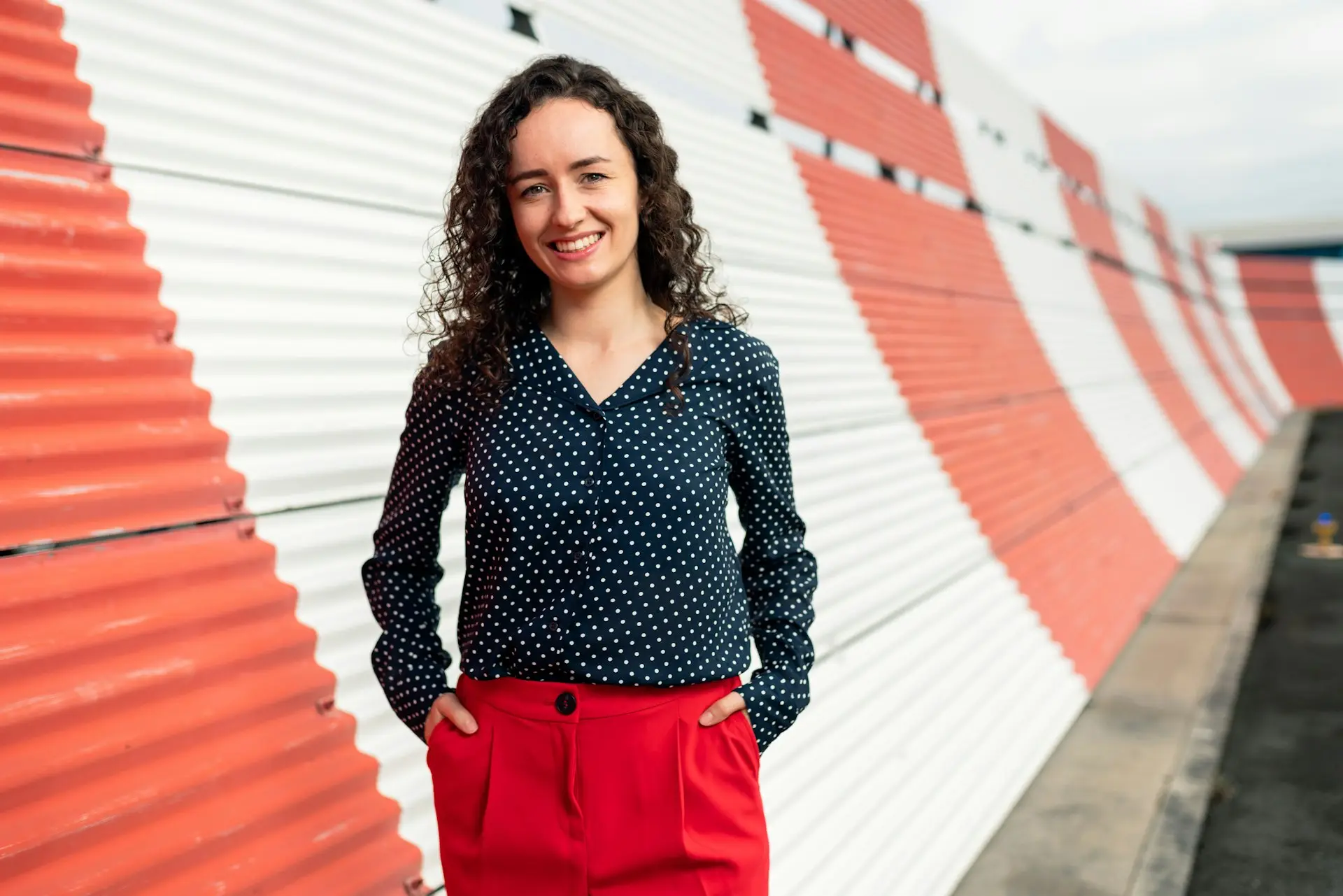 woman in black and white polka dot long sleeve shirt and red skirt standing on sidewalk